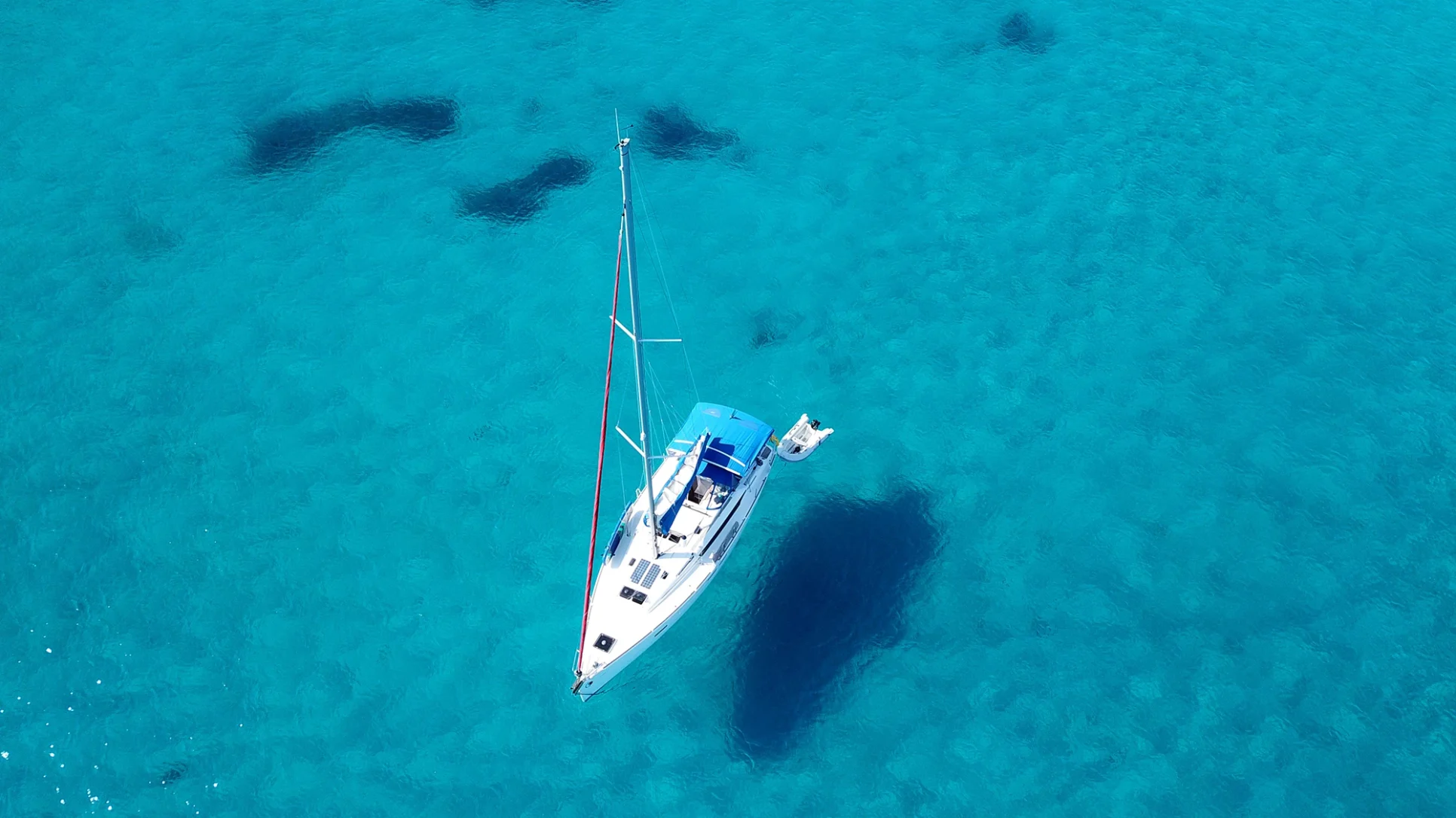 A sailboat gliding on clear blue water under a bright sky, creating a serene and peaceful scene.
