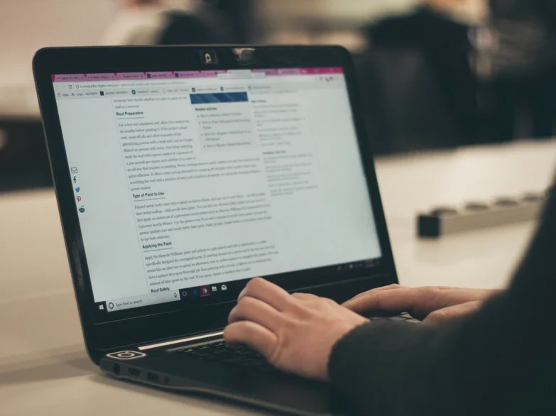 A person typing on a laptop, focused on their work with hands on the keyboard and a screen in front of them.