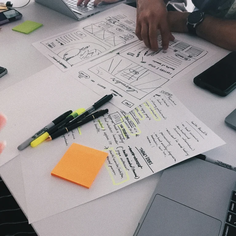 Two people gathered around a table, engaged in content planning with paper and pens.