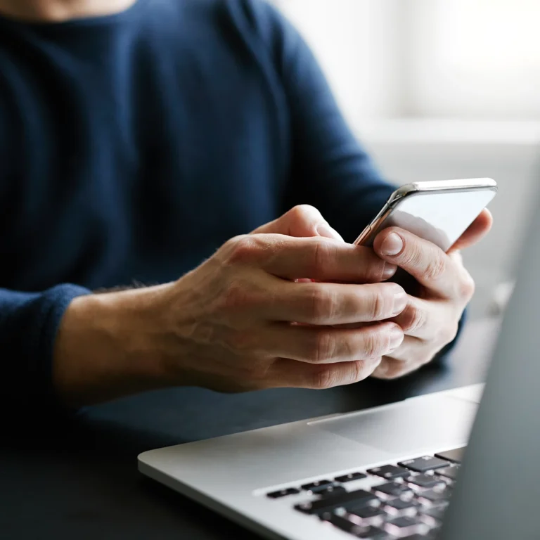 A man sitting at a desk is focused on his phone while working.