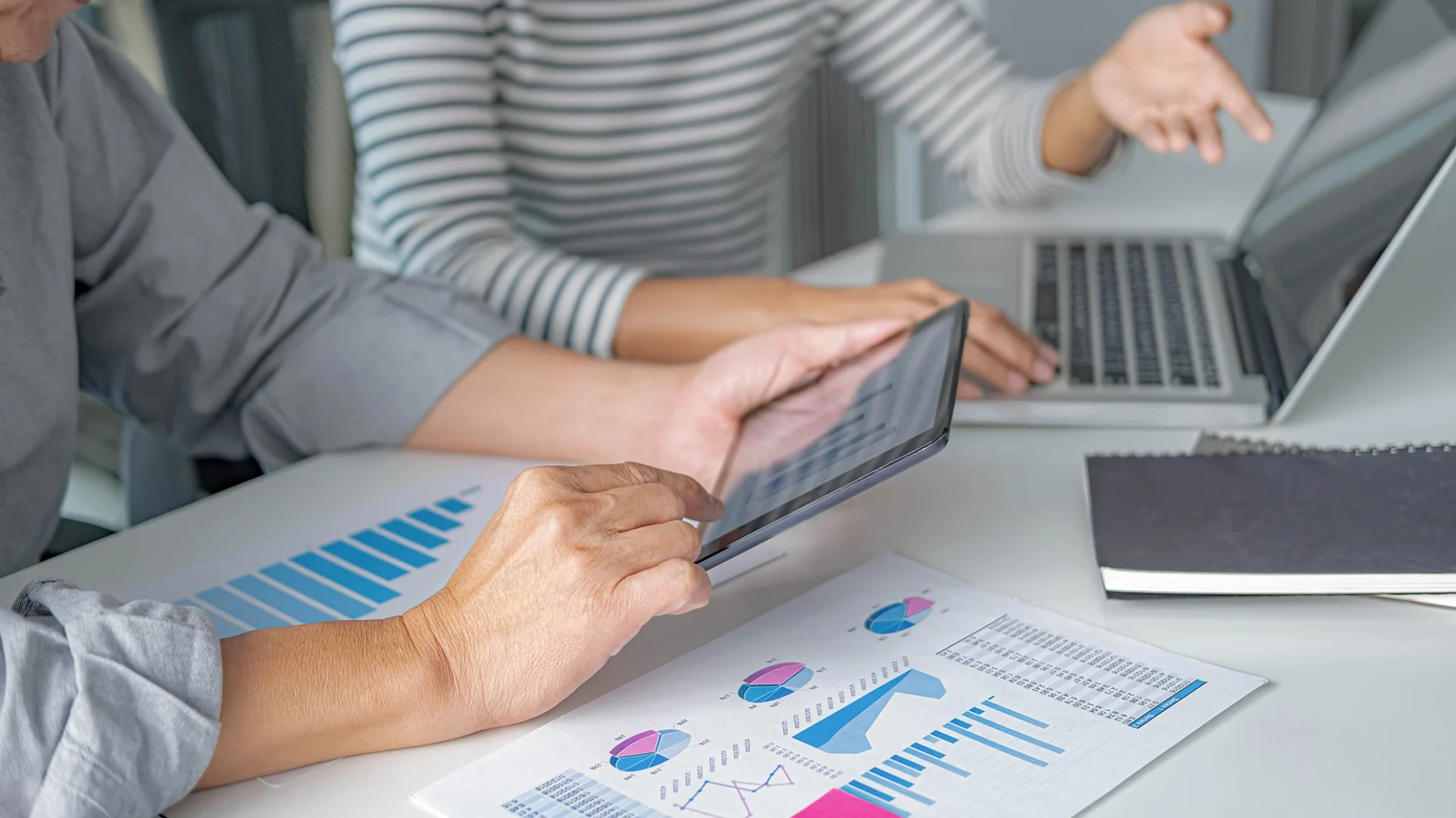 A man and woman sit at a table, focused on a laptop, engaged in collaboration.