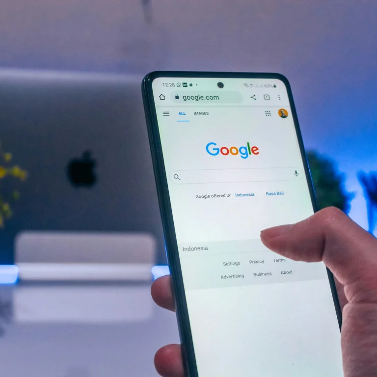 A hand holding a mobile phone with Google search on the screen.