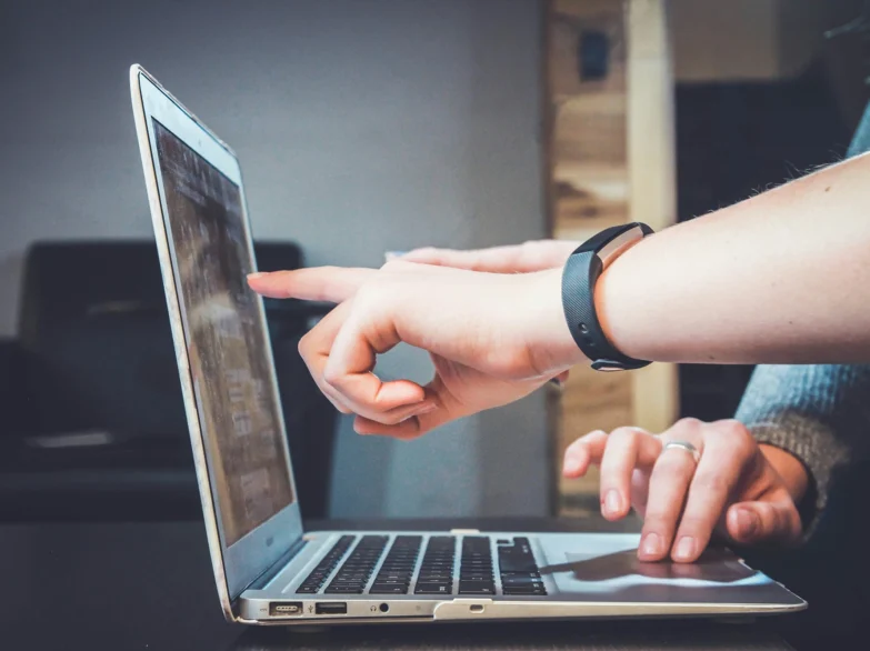 A person pointing at a laptop computer, indicating something on the screen.