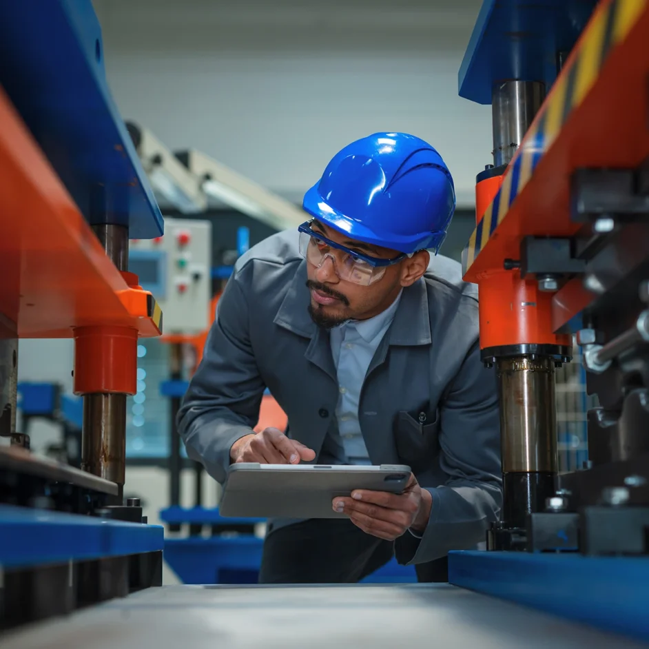 A man wearing a hard hat and glasses is focused on using a tablet.