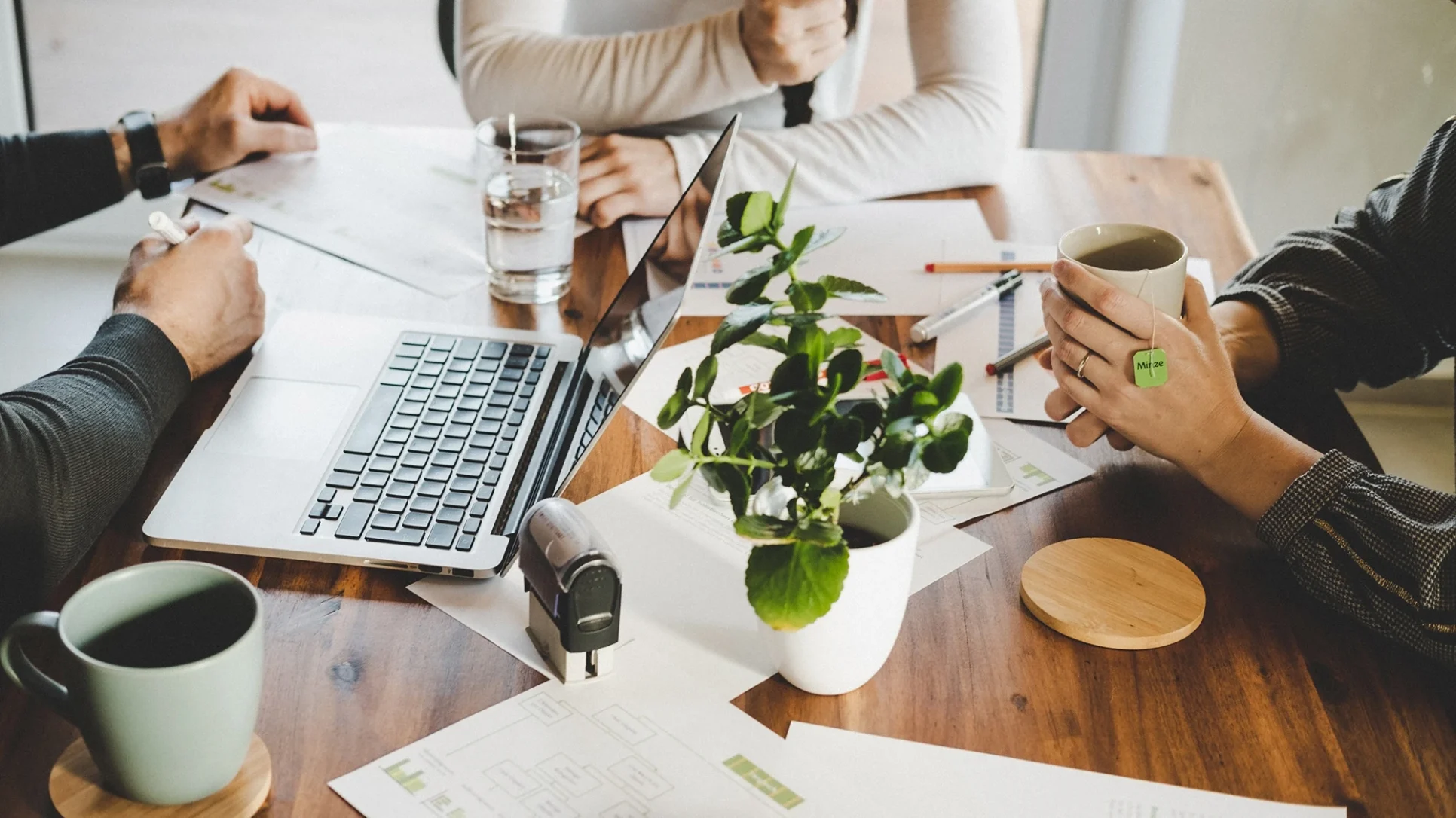 Three people collaborate at a table, using laptops and reviewing papers during a productive meeting.