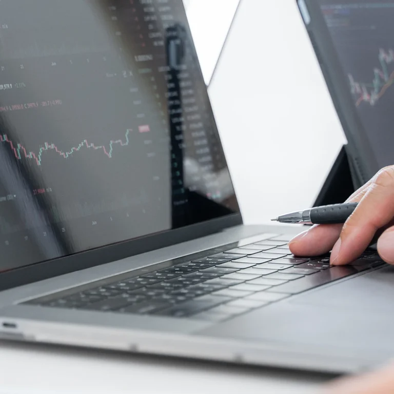 A person analyses graphs on a laptop while taking notes with a pen.