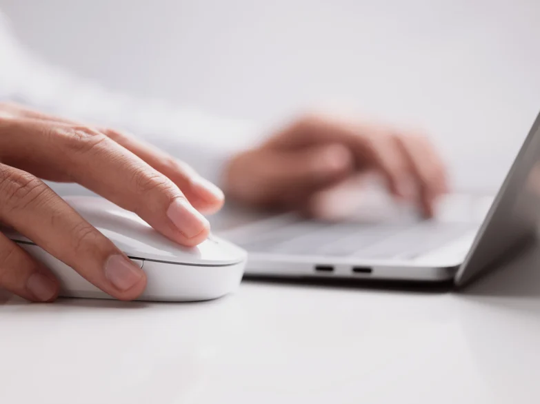 A person using a mouse while working on a laptop, focused on the screen and engaged in their task.