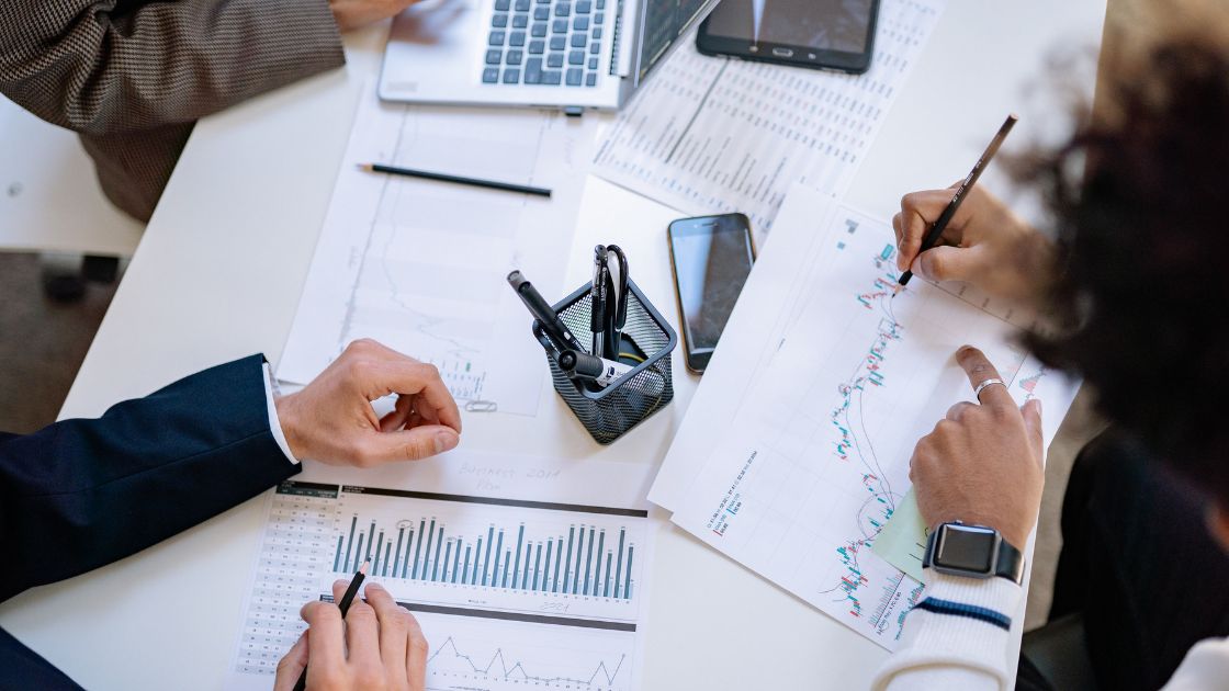 business professionals around a desk, with forecasting charts