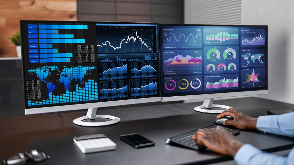 Professional working at a desk with two monitors working on graphs and analytics